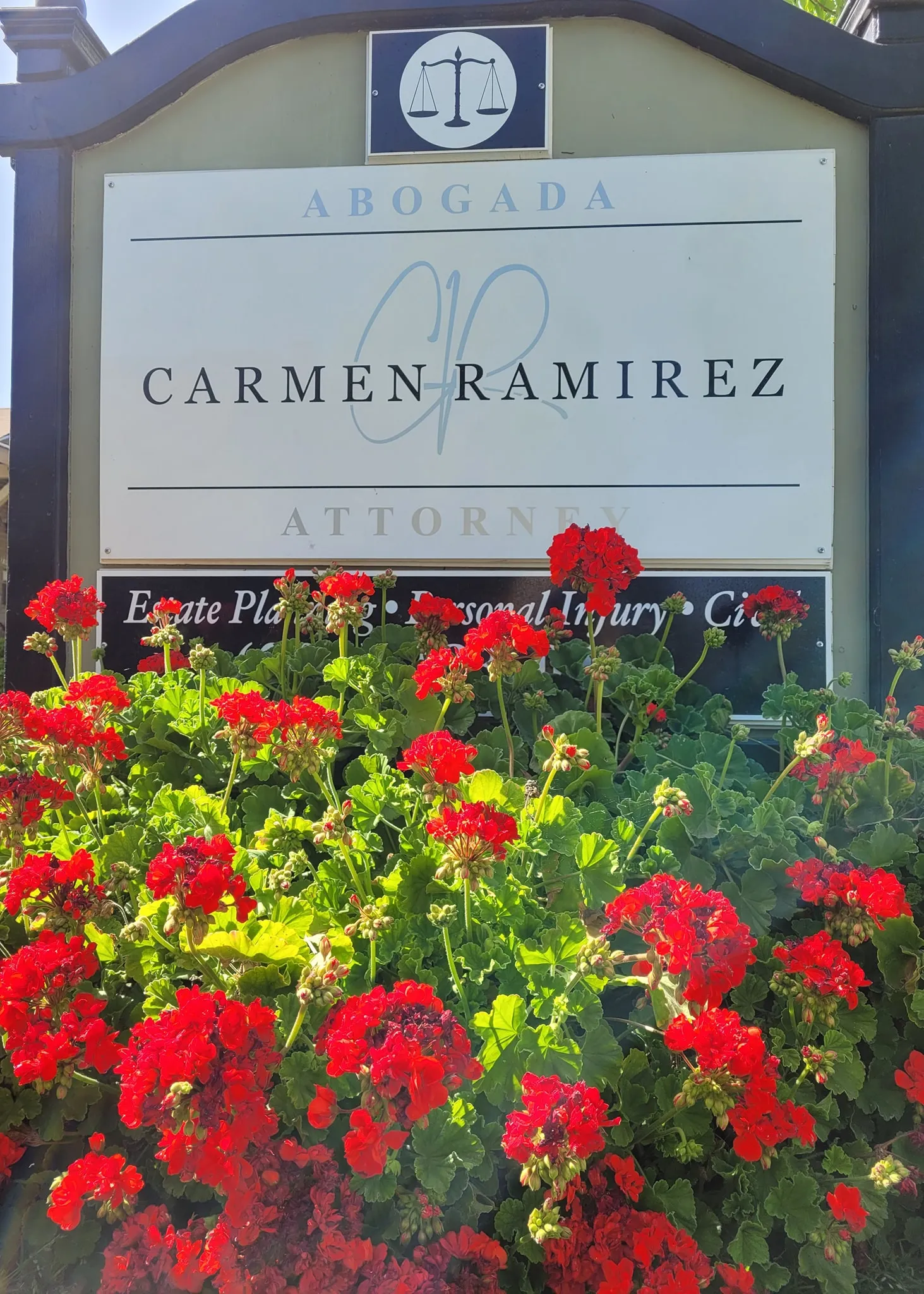 Outdoor sign for Carmen Ramirez Attorney with red flowers in the foreground